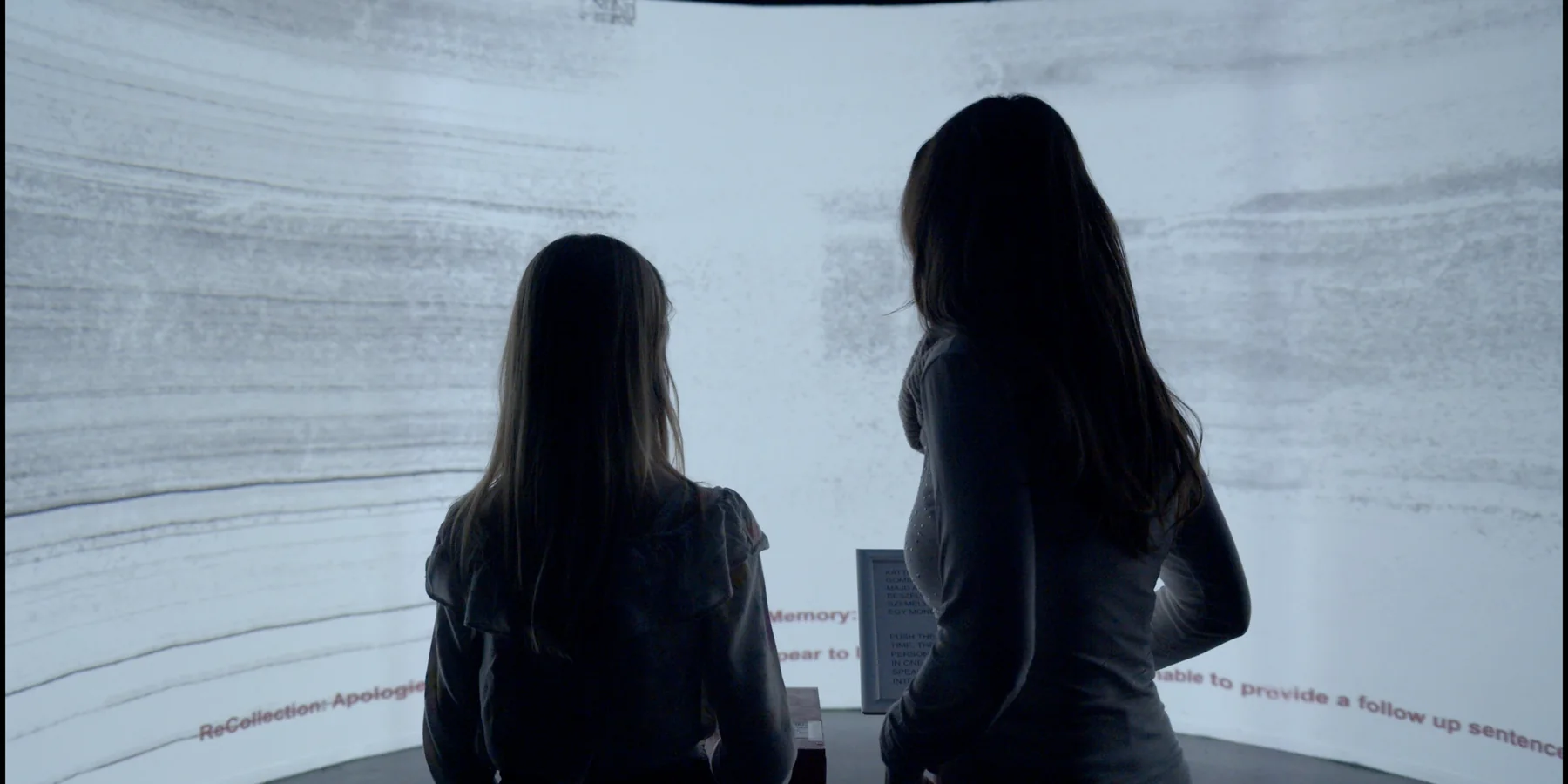 Two visitors stand inside a curved immersive projection