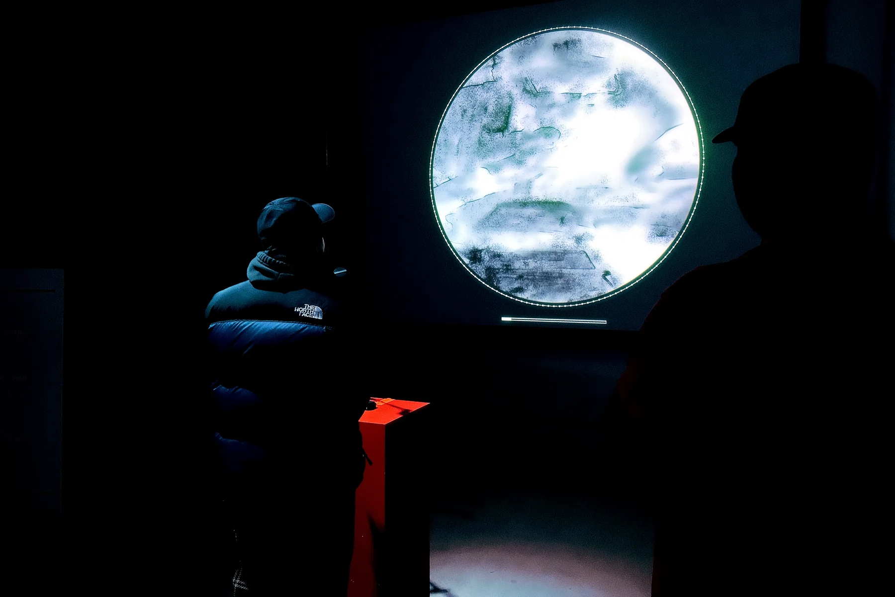 Visitors stand near the circular screen and red podium